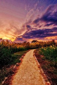 Road amidst field against sky during sunset