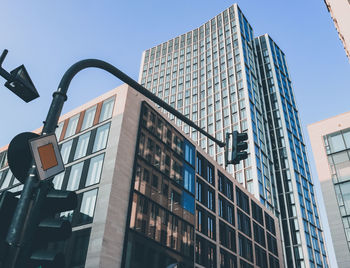 Low angle view of modern buildings with traffic light against clear sky 