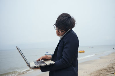 Man using mobile phone at beach against sky