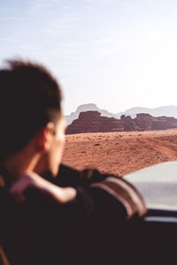 Rear view of man sitting on car against sky