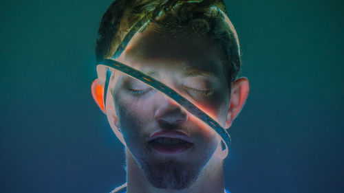 Man with illuminated lighting equipment wrapped on face against colored background