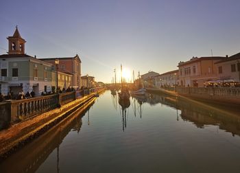 Reflection of buildings on river against sky during sunset