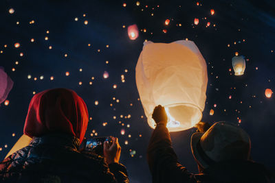 Rear view of people holding illuminated lanterns at night