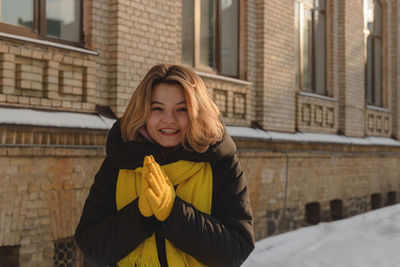 Beautiful happy blonde girl with a yellow scarf and gloves smiling and looking at the camera.