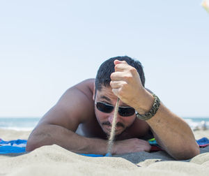 Man spilling sand at beach against clear sky