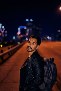 Young man looking away while standing on street at night