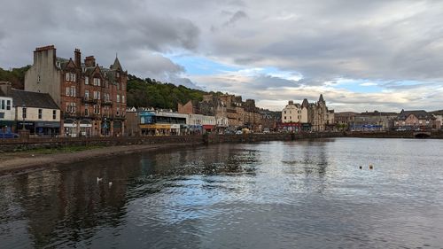 Buildings by river against cloudy sky