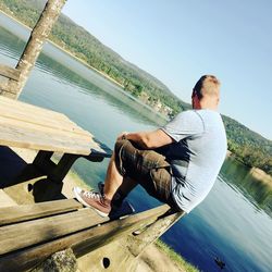 Man on retaining wall by sea against clear sky