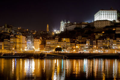 Illuminated buildings by river against sky at night