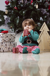 A little 12-month-old christmas elf with a christmas tree and gifts