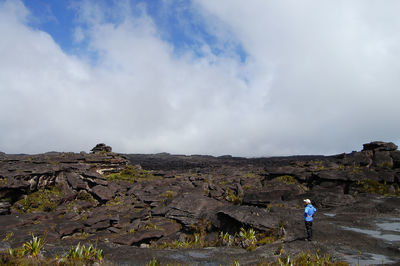 Man standing on rocky shore against cloudy sky