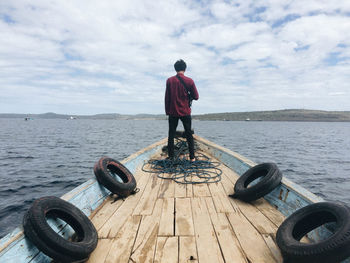 Rear view of man standing on boat at the sea against sky