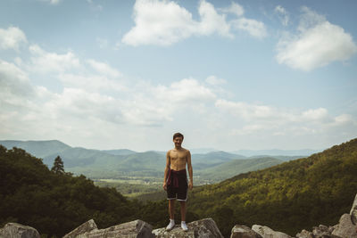 Full length of shirtless man standing on rock against sky