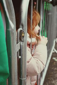 Girl looking away while standing by fence