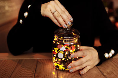 Midsection of woman holding coin in jar on table