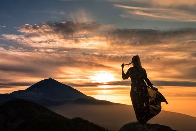 Silhouette woman standing on mountain against orange sky