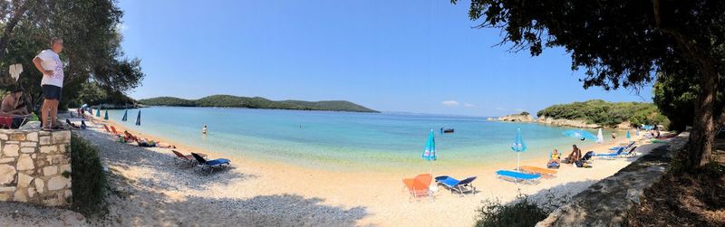 Panoramic view of people on beach against clear blue sky