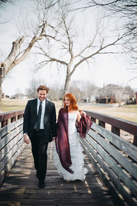 Couple walking on footbridge against bare trees