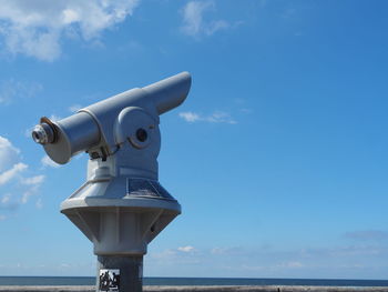 Low angle view of coin-operated binoculars by sea against sky