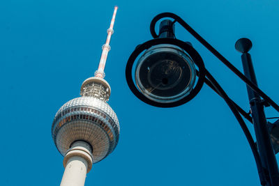 Low angle view of fernsehturm and street light against clear blue sky