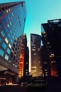 Illuminated modern buildings in city against clear sky at dusk