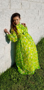 Full length of woman in green floral dress leaning on stone wall
