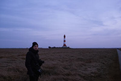 Young woman standing on field by lighthouse against sky