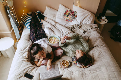 High angle view of female friends spending leisure time on bed at home