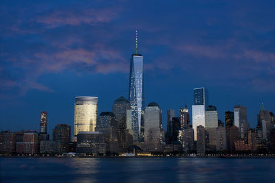 Illuminated buildings in city against cloudy sky