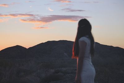 Rear view of woman standing against sky during sunset