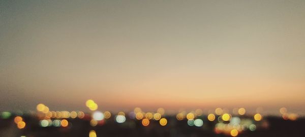 Defocused image of illuminated cityscape against sky at sunset