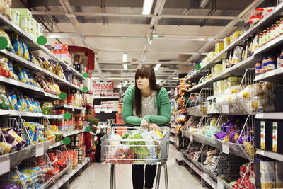 Young woman leaning on shopping cart at supermarket aisle