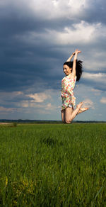 Full length excited young woman jumping on grassy field