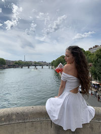 Rear view of woman drinking beverage against river