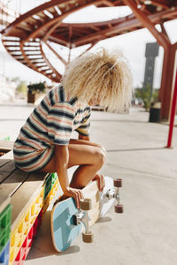 Mid adult woman with blond curly hair holding skateboard while sitting on wooden seat