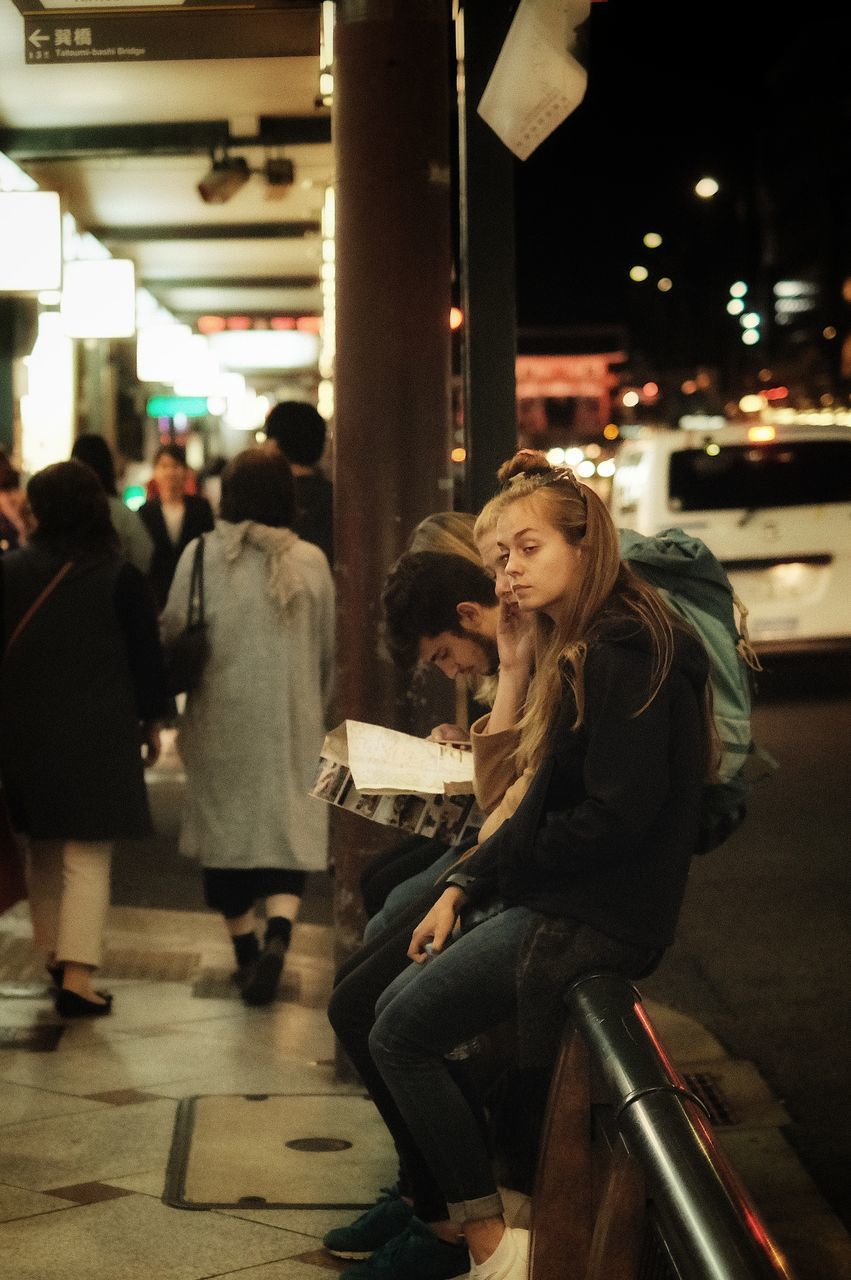 SIDE VIEW OF CROWD SITTING IN CITY AT NIGHT