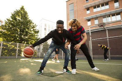 Male friends with playing basketball in sports field