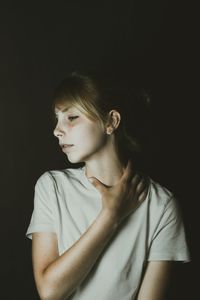 Young woman touching neck over black background