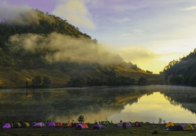 People by lake against sky during sunset