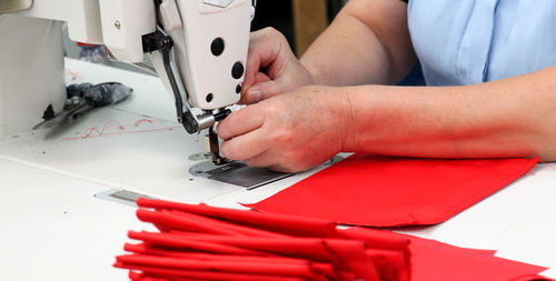 Midsection of tailor using sewing machine while stitching red textile