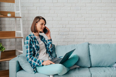 Young man using mobile phone while sitting on sofa at home