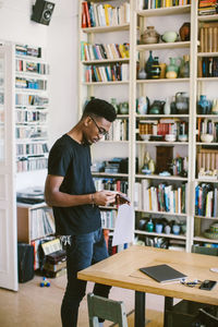 Young man reading paper while standing by table at home