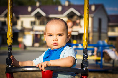 Serious cute baby boy at the swing at children playground
