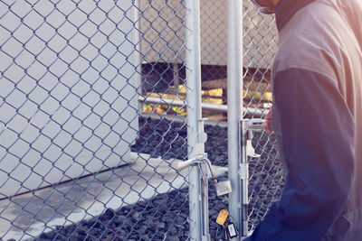 Rear view of man standing by chainlink fence