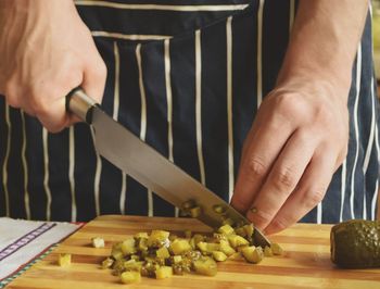 Midsection of chef cutting pickled cucumber with knife on table