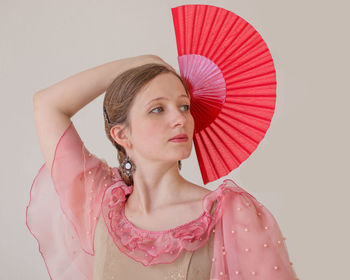 Portrait of a beautiful young woman on a white background dancing flamenco with a red fan 