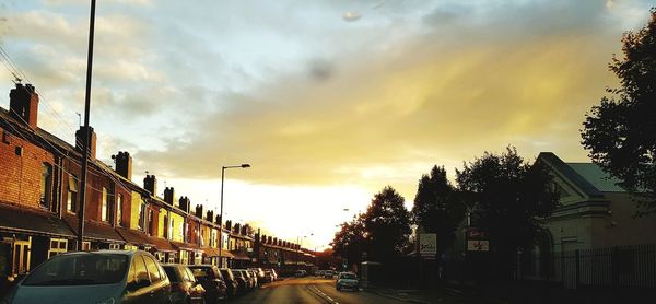 Cars on road by buildings against sky during sunset