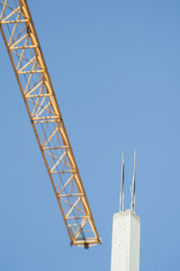 Low angle view of concrete column at and crane incomplete building against clear sky