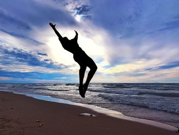 Silhouette man jumping on beach against sky during sunset