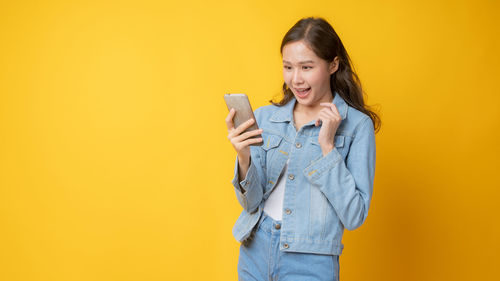 Smiling young woman standing against yellow background